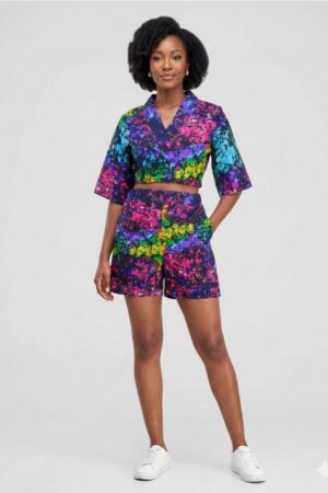 A beautiful model wearing a vibrant African print two piece set featuring a multi-colored abstract batik crop top and matching tailored high-waisted shorts.